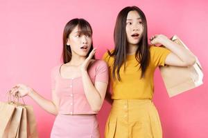 retrato de duas lindas meninas asiáticas segurando muitas sacolas de compras no fundo rosa