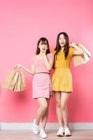 retrato de duas lindas meninas asiáticas segurando muitas sacolas de compras no fundo rosa