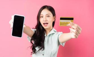 jovem mulher asiática segurando um telefone celular enquanto segura um cartão do banco na mão