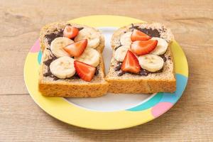 pão integral torrado com banana fresca, morango e chocolate no café da manhã foto