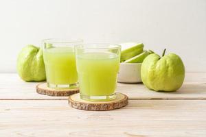 Copo de suco de goiaba fresco com goiaba fresca na mesa de madeira foto