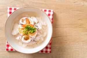 mingau ou sopa de arroz cozido com frutos do mar de camarão, lula e peixe em uma tigela foto