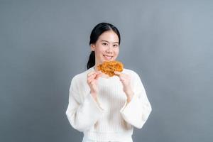 jovem mulher asiática vestindo um suéter com uma cara feliz e gosta de comer frango frito no fundo cinza foto