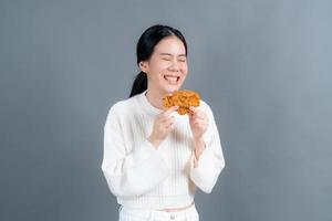 jovem mulher asiática vestindo um suéter com uma cara feliz e gosta de comer frango frito no fundo cinza foto