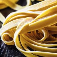 fechar acima do uma cru seco italiano massa fettuccine em Preto de madeira mesa. ai generativo foto