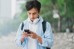 jovem asiático usando mochila e olhando para a tela do telefone foto