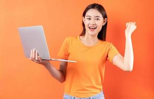 jovem mulher asiática segurando laptop na mão com expressão de vitória foto