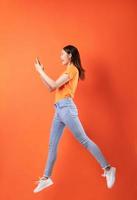 jovem mulher asiática vestindo uma camiseta laranja pulando em um fundo laranja