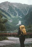 caminhante com mochilas com kappa ponte Kamikochi com rio e okuhotaka dia montanha fundo. Kamikochi famoso Lugar, colocar para caminhada e caminhada dentro matsumoto, Nagano, Japão foto