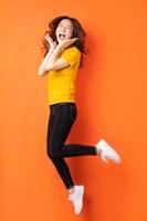 jovem asiática pulando em um fundo laranja foto
