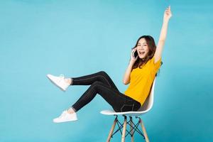 jovem asiática sentada na cadeira usando o telefone com uma expressão alegre no fundo foto