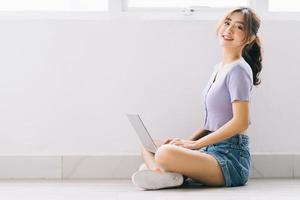 linda garota asiática sentada no chão e usando o laptop em casa