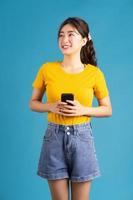 jovem mulher asiática em pé e usando o smartphone sobre fundo azul foto