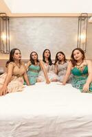 uma grupo do ásia mulheres dentro lindo vestidos sentado juntos em uma branco cama enquanto ficando foto