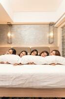 uma grupo do ásia mulheres estão dormindo e inclinado em branco almofadas com seus amigos dentro uma luxo hotel foto