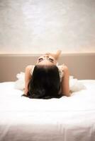 a ásia mulher com Preto cabelo é dormindo em uma branco cama dentro a elegante hotel foto