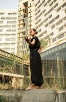 a ásia homem posando dentro uma Preto traje dentro frente do uma alto, imponente construção foto