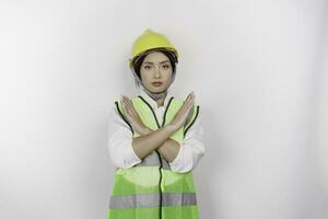 lindo ásia mulher trabalho trabalhador vestindo uma segurança capacete e colete com mão gesticulando rejeição ou proibição isolado branco fundo. trabalho dia conceito. foto