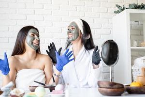 duas lindas mulheres em luvas aplicando máscara facial se divertindo