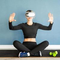 jovem loira com roupas esportivas e óculos de realidade virtual, sentada no tapete de fitness usando o menu interativo de VR
