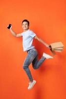 homem asiático segurando um smartphone e uma sacola de compras enquanto pula foto