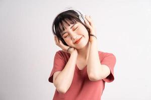 jovem asiática usando fones de ouvido sem fio para ouvir música no fundo branco foto