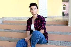 linda mulher afro-americana com cabelo curto, sentado na escada do lado de fora, estilo de vida foto