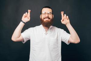 foto de jovem barbudo hipster de camisa branca cruzando os dedos e fazendo um pedido