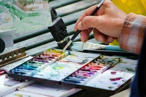 uma do homem mão segurando a pincel e mistura cor em pintura paleta, dentro fechar acima foto
