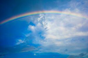 lindo multicolorido arco Iris depois de chuva em a azul céu e branco nuvens. foto