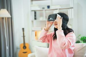 ásia mulher sorrir e jogar vr jogo, 3d dispositivo Novo inovação óculos para entreter dentro vivo quarto às lar, ásia mulher alegre dentro casa em feriado. feliz mulher jogando metaverso vr tecnologia conceito. foto