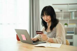 mulher segurando mostrando o cartão de crédito para fazer compras online. mulher asiática trabalhando em casa. compras on-line, e-commerce, internet banking, gastar dinheiro, trabalhar em casa. foto