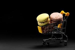 macarons de biscoitos de amêndoa coloridos ou macaroons no carrinho de compras em fundo preto. minimalismo, sombras nítidas