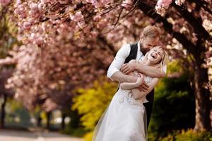 lindo casal jovem, homem com barba e mulher loira, abraçando-se no parque primavera. casal elegante perto da árvore com sakura. conceito de primavera. moda e beleza
