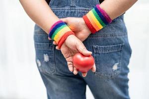 senhora asiática usando pulseiras de bandeira de arco-íris e segurar um coração vermelho, símbolo do mês do orgulho LGBT, comemorar anual em junho social de gays, lésbicas, bissexuais, transgêneros, direitos humanos.
