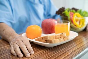 paciente asiático sênior ou idosa idosa comendo alimentos saudáveis de vegetais de café da manhã com esperança e feliz enquanto está sentado e com fome na cama no hospital.