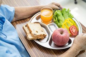 paciente asiático sênior ou idosa idosa comendo alimentos saudáveis de vegetais de café da manhã com esperança e feliz enquanto está sentado e com fome na cama no hospital. foto