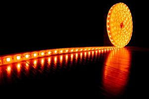 Fita decorativa de diodo para iluminação, um rolo de tira de led com luz quente amarela no piso laminado foto