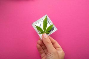proteção no sexo ao usar drogas, preservativo e folha de cannabis em fundo rosa foto
