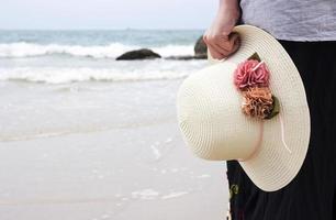 jovem segurando chapéu na praia foto