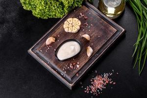 molho de alho em molho de cerâmica preta com folhagem em uma tábua de madeira foto