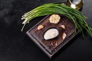 molho de alho em molho de cerâmica preta com folhagem em uma tábua de madeira foto