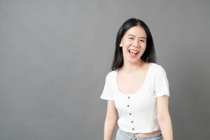 jovem mulher asiática com rosto feliz e sorridente em uma camisa branca em fundo cinza foto