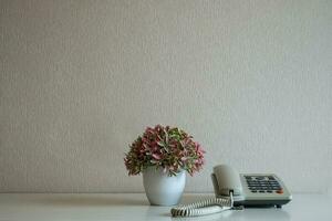 telefone e vaso de flores na mesa no fundo da parede cinza foto