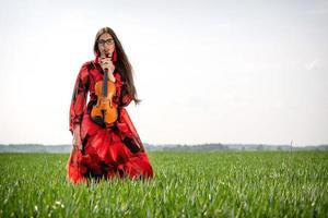 jovem de vestido vermelho com violino em prado verde - imagem foto