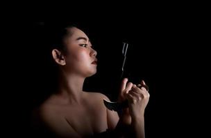 Ásia mulher com uma mão segurando uma arma e uma faca de karambit no fundo preto foto