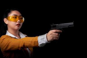 Asea mulher vestindo um terno amarelo com uma das mãos segurando uma pistola em fundo preto foto