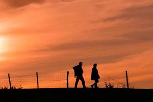 silhueta de um casal caminhando na montanha com um pôr do sol foto