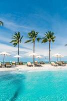 espreguiçadeiras ou camas e guarda-sóis ao redor da piscina com fundo do mar - feriados e conceito de férias foto