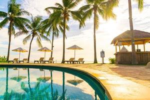 belos guarda-sóis e cadeiras de luxo ao redor de uma piscina ao ar livre em um hotel e resort com coqueiros no céu do pôr do sol ou do nascer do sol - conceito de férias e férias foto